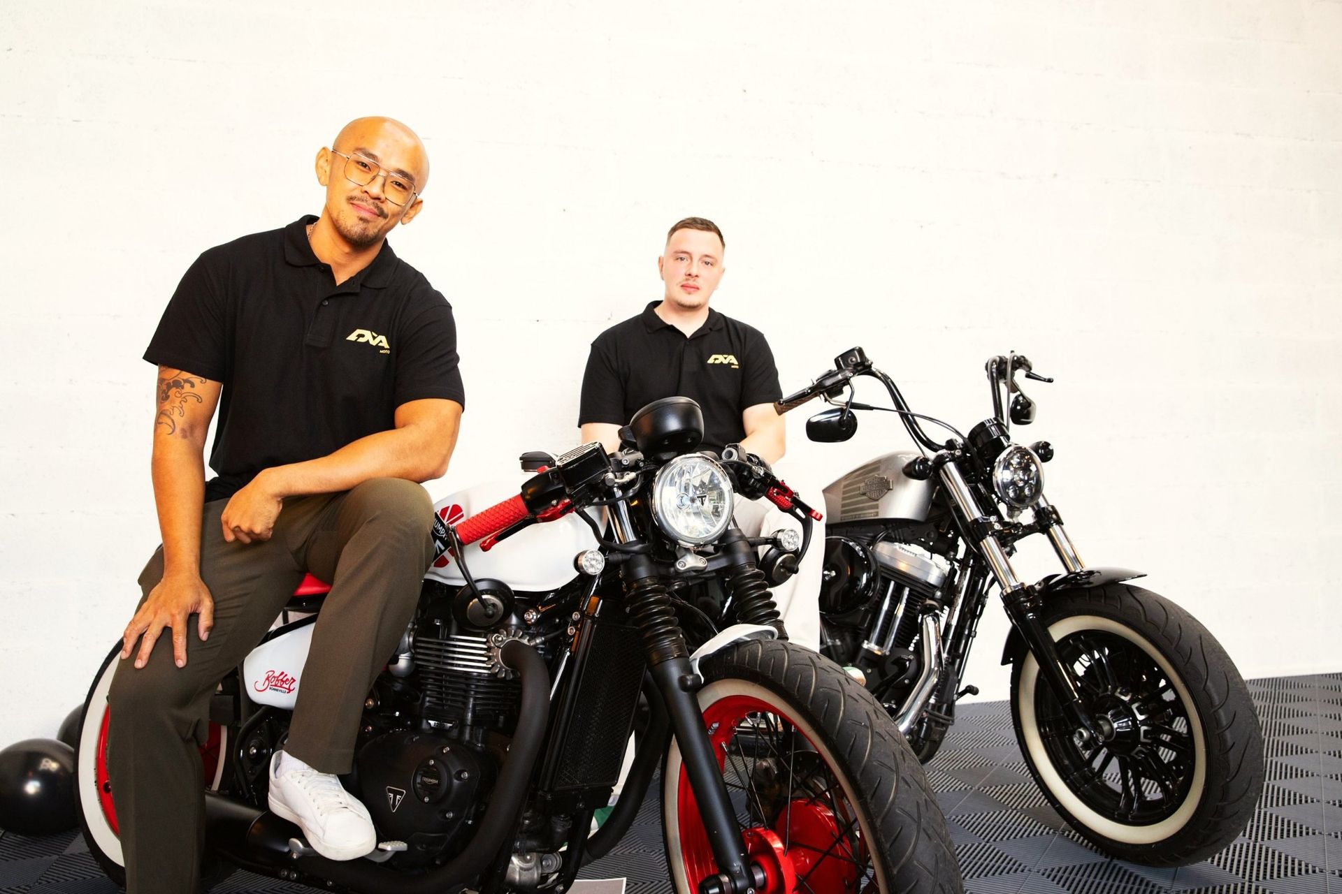 Les deux associés de DVA MOTO dans la boutique, sur une Triumph Bobber et une Harley-Davidson