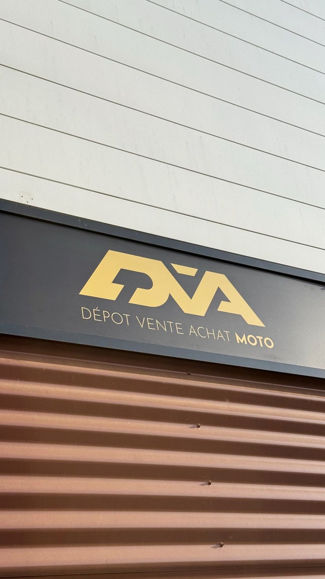 L’enseigne DVA MOTO, logo doré sur fond graphite, au-dessus du rideau de la boutique
